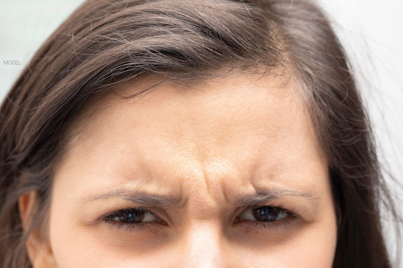 Close up image of a young woman with frown lines on her forehead and between her eyes 
