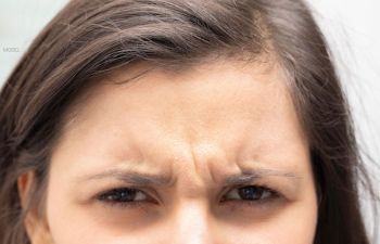 Close up image of a young woman with frown lines on her forehead and between her eyes 